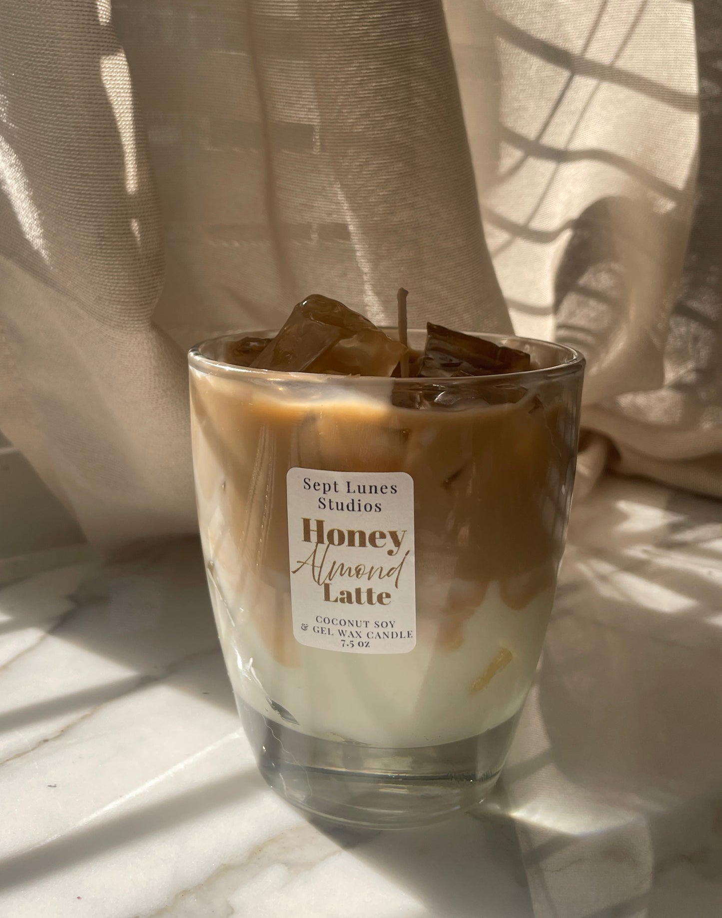 Candle in a glass jar with a label on a light surface, draped with sheer curtains.