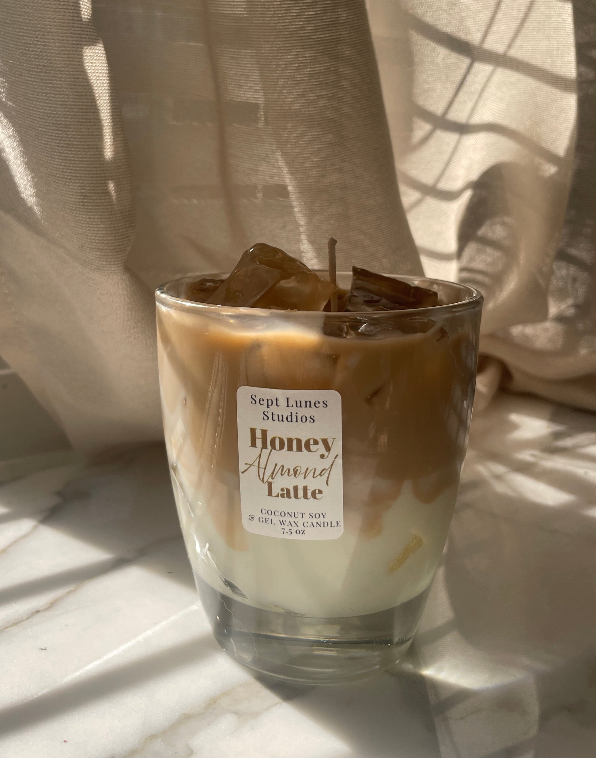 Candle in a glass jar with a label on a light surface, draped with sheer curtains.