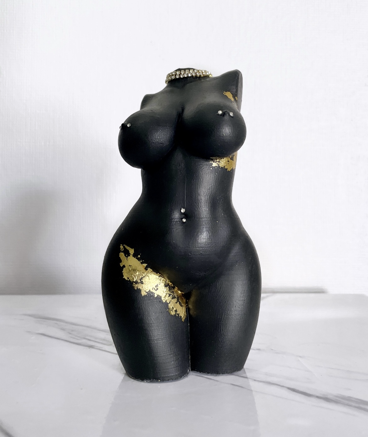 Black and gold decorative object resembling a female torso on a white background