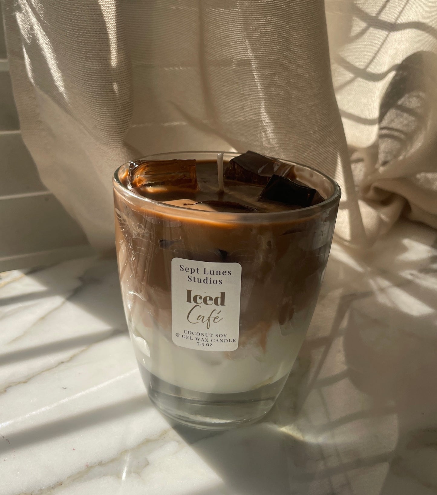 Candle in a glass jar labeled 'Iced Cafe' on a marble surface with a curtain in the background