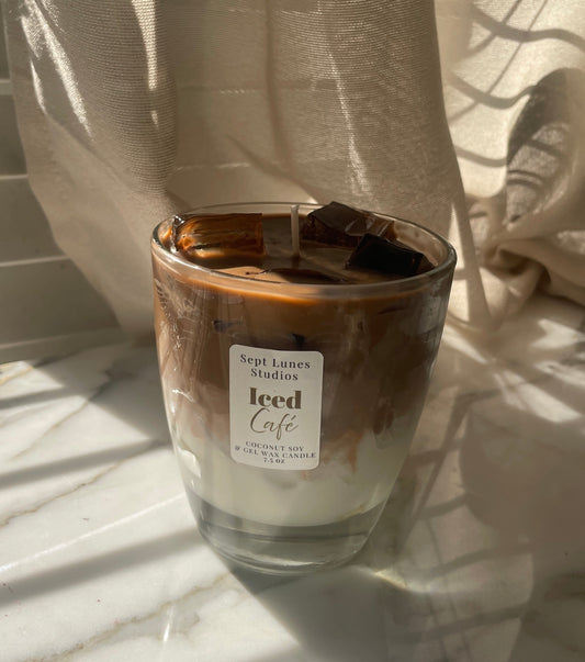 Candle in a glass jar labeled 'Iced Cafe' on a marble surface with a curtain in the background